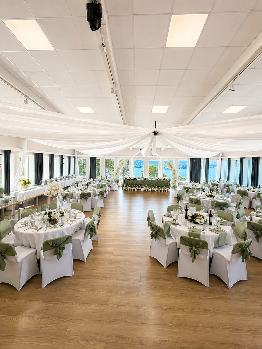 Bryllupslokale med hvite takdraperinger, runde bord og sage green stolsløyfer med sjøutsikt